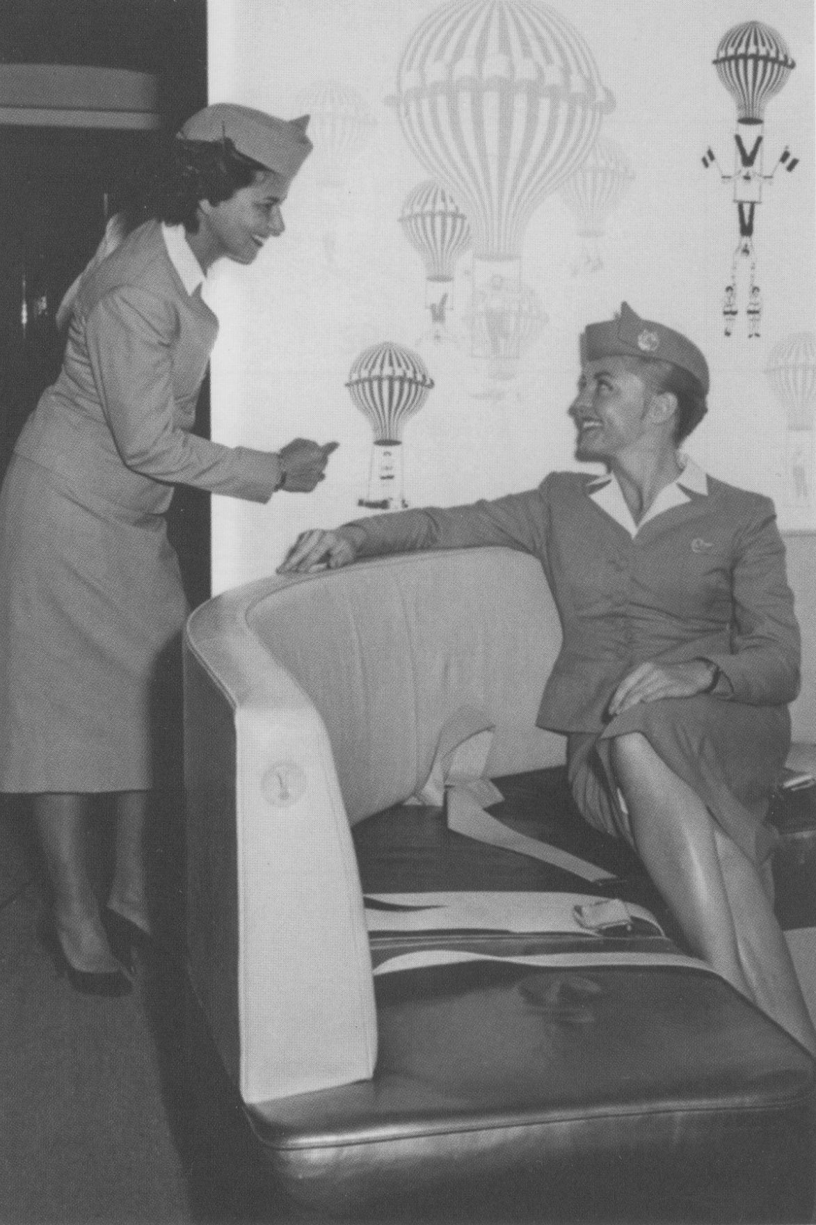 1950s 2 stewardesses await customer boarding in the First Class lounge of a Boeing 707.